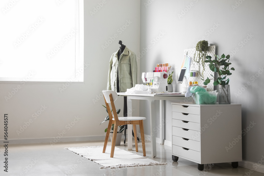 Tailors workplace with sewing machine, pegboard and tablet computer in atelier