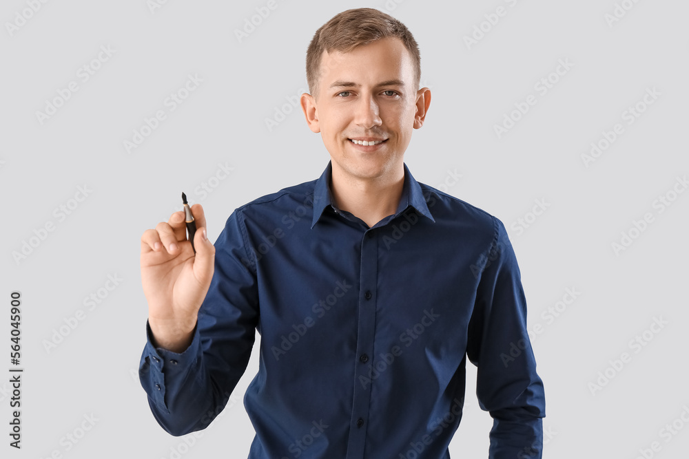 Young businessman with pen on light background