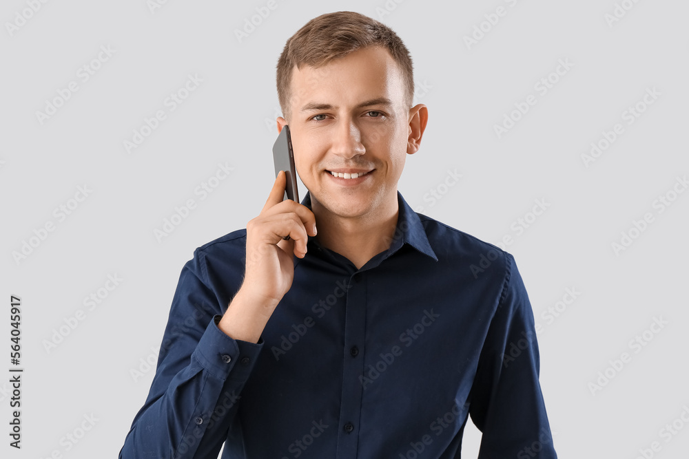 Young businessman in blue shirt talking by mobile phone on light background