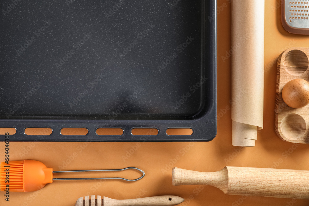 Baking tray with utensils on orange background