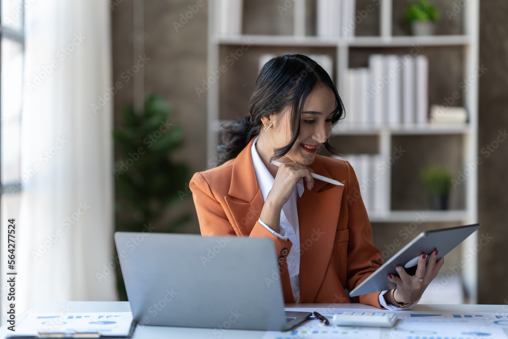 聪明的亚洲女商人在办公室做项目时拿着平板电脑。