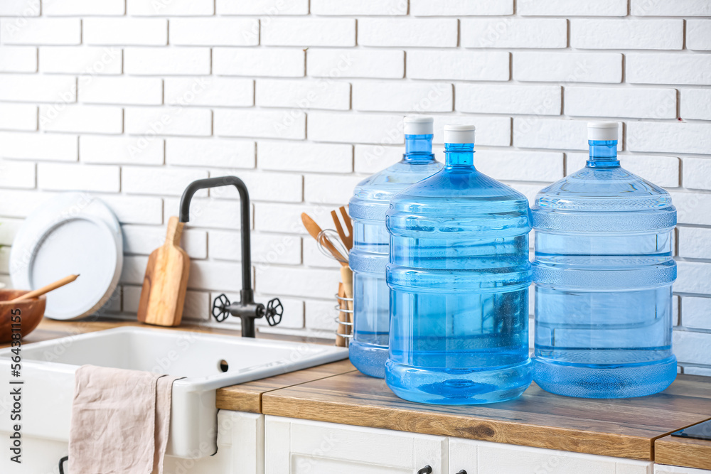 Bottles of clean water and sink on kitchen counter near white brick wall