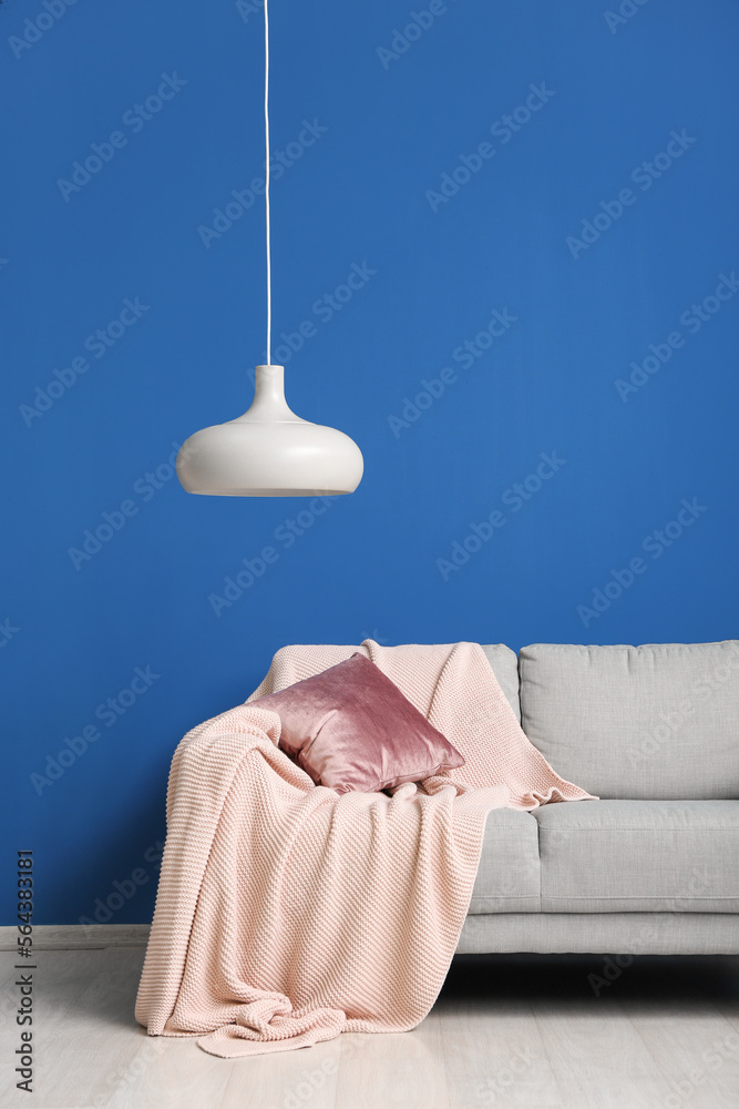 Grey sofa with cushion, plaid and hanging lamp near blue wall