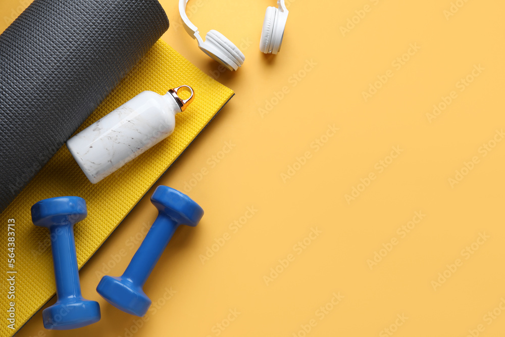 Sports water bottle with dumbbells, headphones and mat on orange background