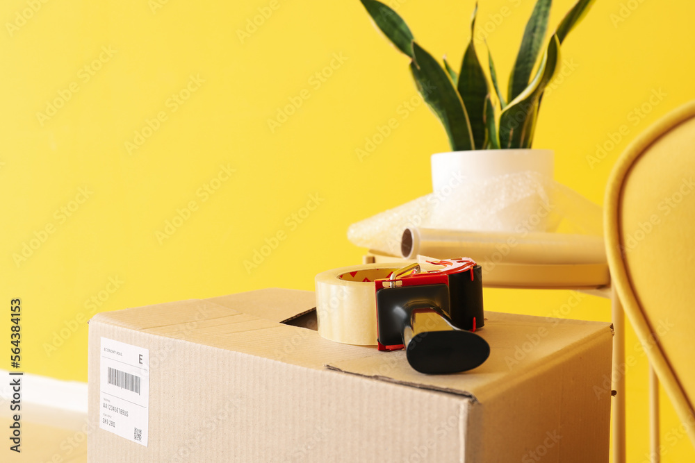 Cardboard box with adhesive tape in living room on moving day, closeup