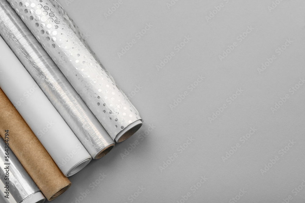 Rolls of aluminium foil and baking paper on grey background, closeup