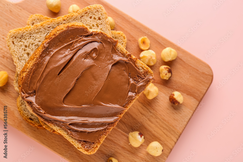 Wooden board of tasty toasts with hazelnut butter on pink background, closeup