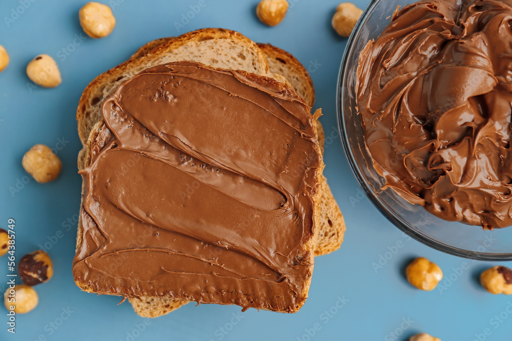 Composition with tasty toasts, bowl of hazelnut butter and nuts on color background, closeup