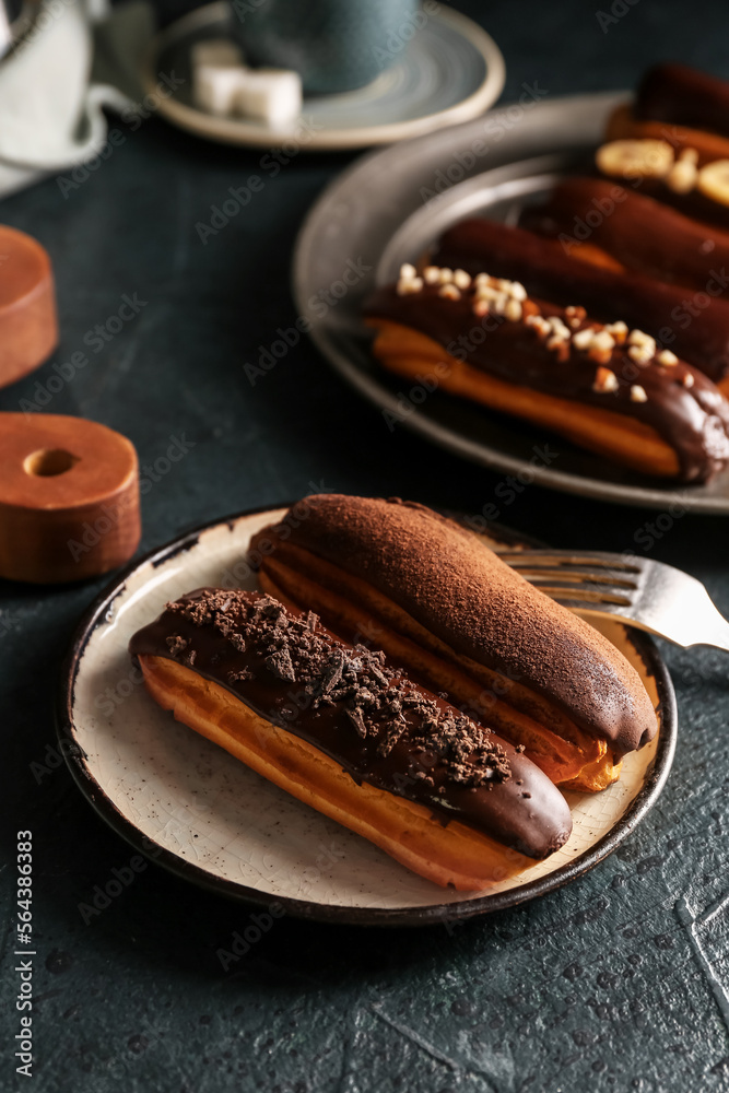 Plates of sweet chocolate eclairs on dark color background, closeup