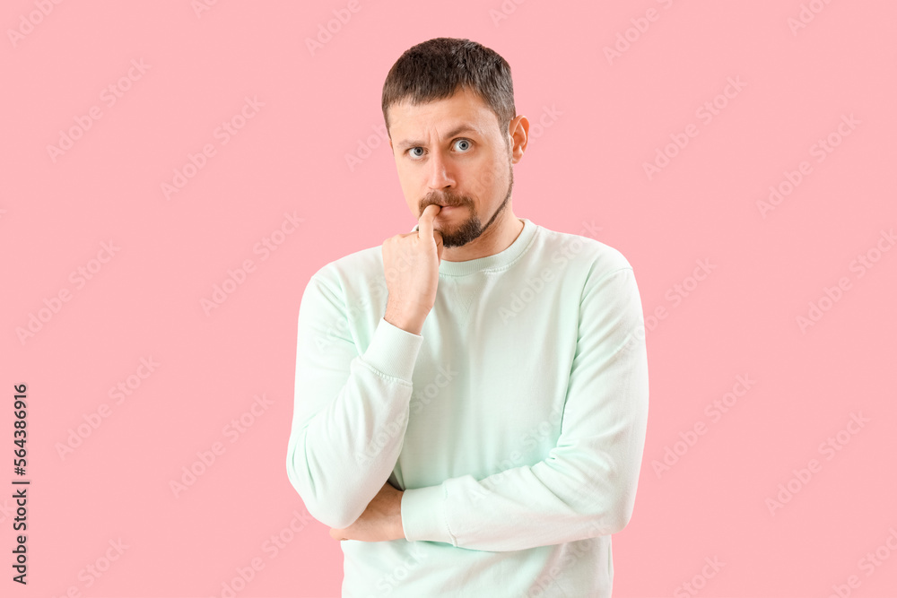 Handsome man biting nails on pink background