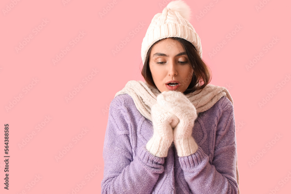 Frozen young woman in winter clothes on pink background