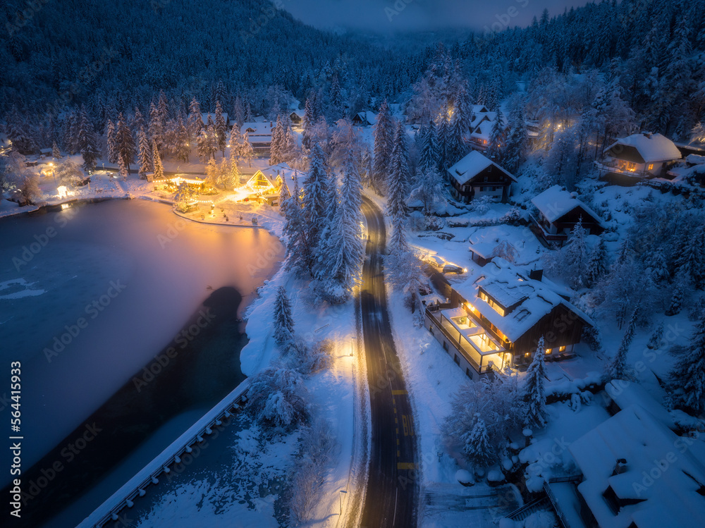 Aerial view of fairy town in snow, road, forest, Jasna lake and houses with lights at night in winte