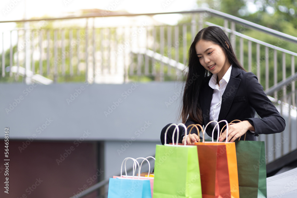 年轻漂亮的亚洲女人拿着五颜六色的购物袋在城市里行走。带着shopp的快乐女人