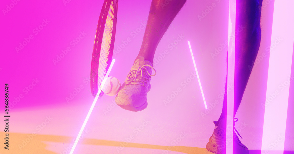 Low section of african american male tennis player with racket kicking ball over illuminated lines