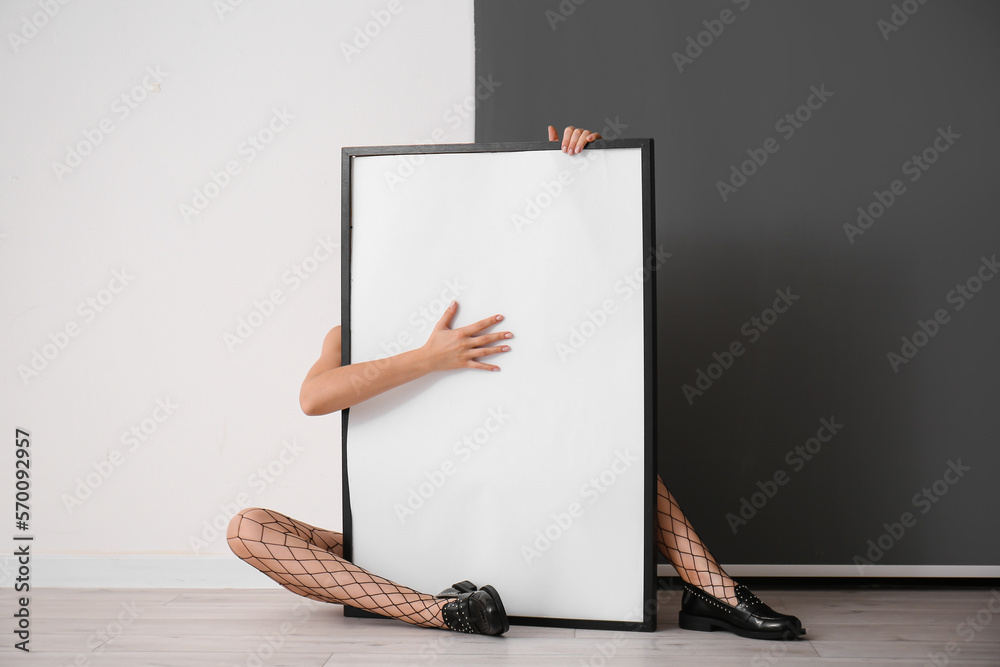 Woman in fishnet tights with blank frame sitting near black and white wall