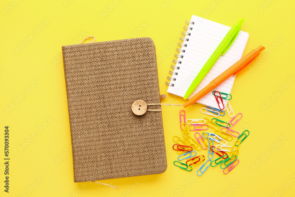 Notebooks, pens and paper clips on yellow background