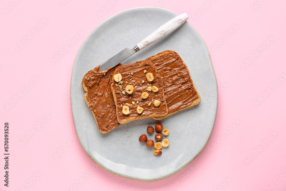 Plate of tasty toasts with hazelnut butter and nuts on pink background