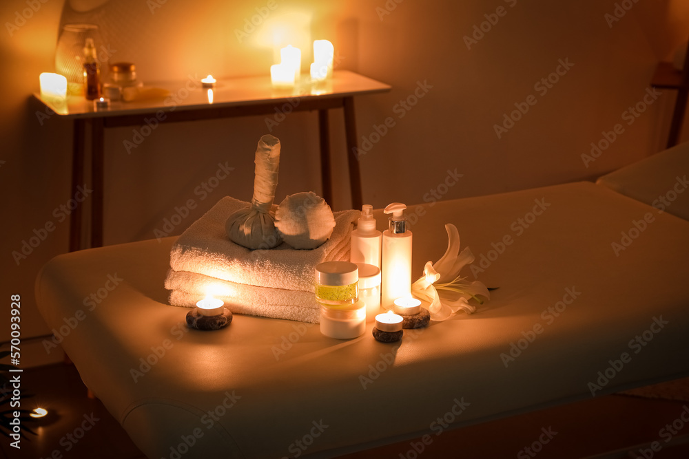 Spa composition with lily flower and burning candles on couch in dark salon