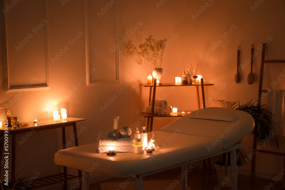 Interior of dark spa salon with couch, burning candles and table