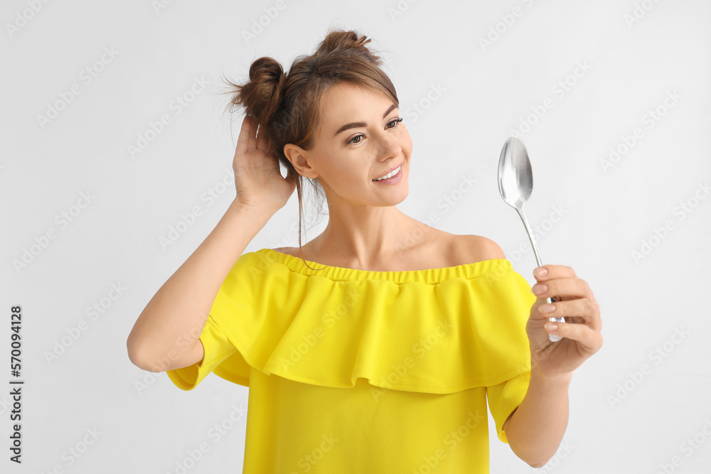 Beautiful woman with silver spoon on light background