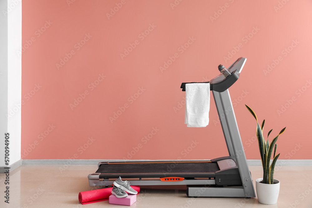 Interior of room with modern treadmill and towel near pink wall