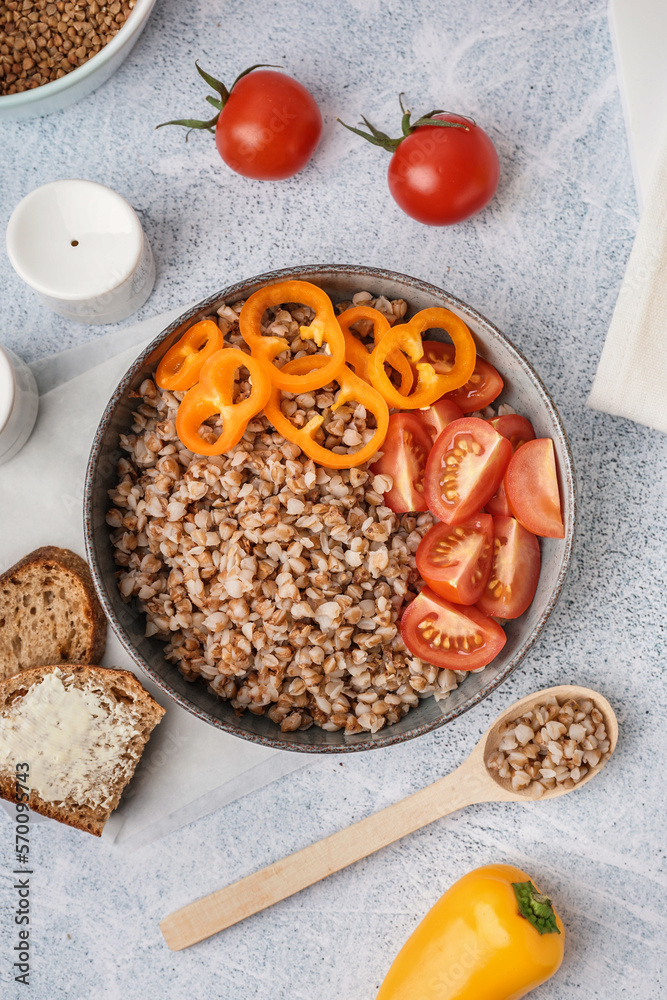 Bowl of tasty buckwheat porridge with fresh vegetables and bread on grey table