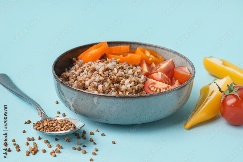 Bowl of tasty buckwheat porridge with fresh vegetables on blue background