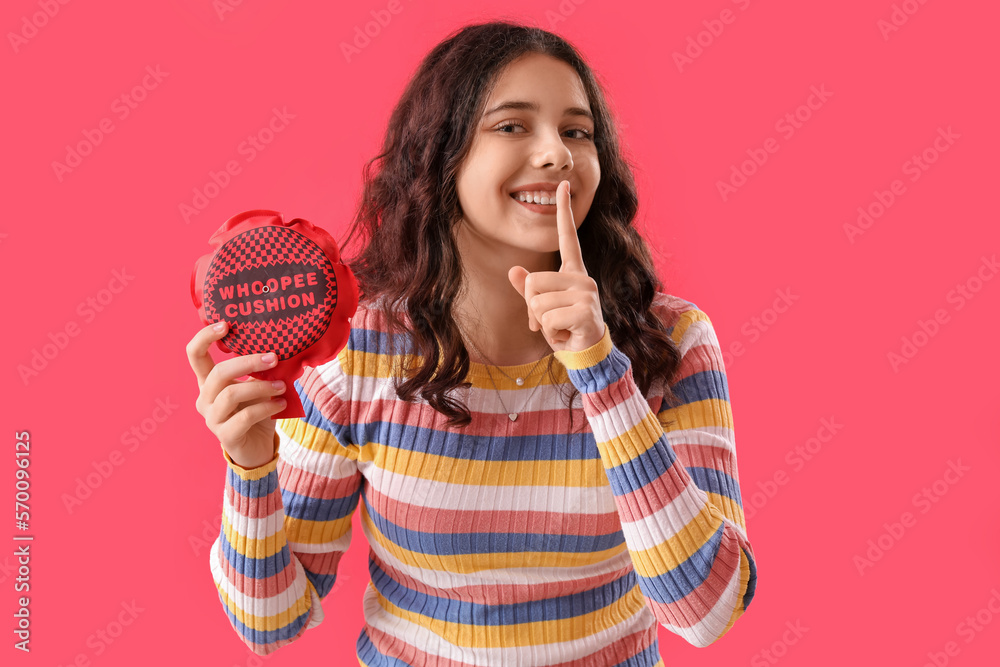 Teenage girl with whoopee cushion showing silence gesture on red background. April Fools Day celebr