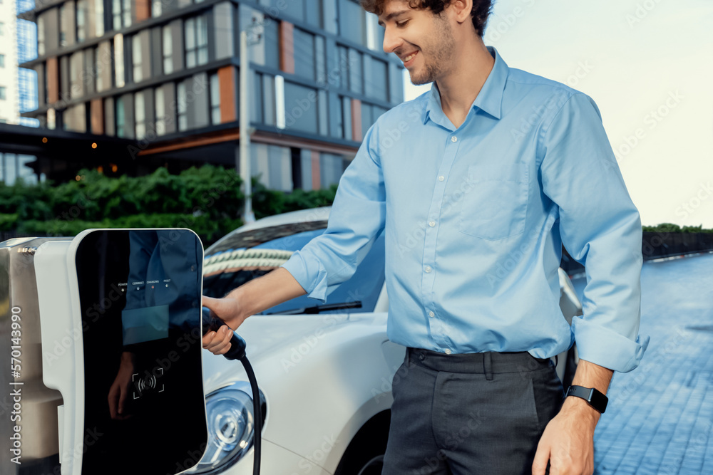 Progressive businessman insert charger plug from charging station to his electric vehicle with apart