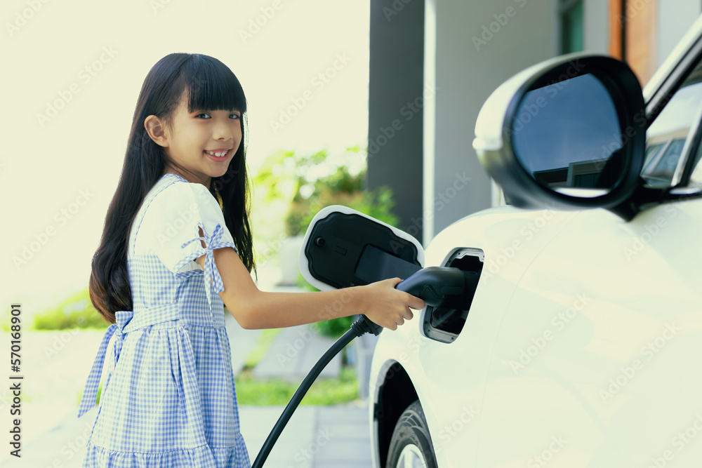 A playful girl holding an EV plug, a home charging station providing a sustainable power source for 