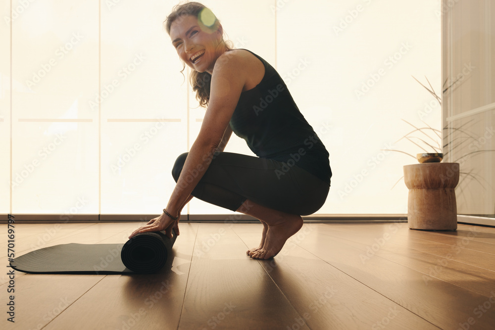 Mature woman smiling while folding up an exercise mat at home