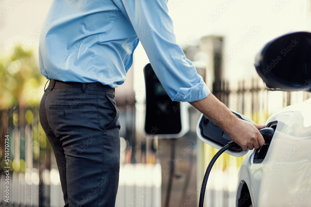 Closeup progressive man holding EV charger plug from public charging station for electric vehicle wi