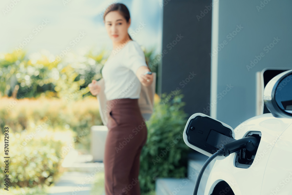 Focus EV charger plugged into EV car at home charging station with blurred background of progressive