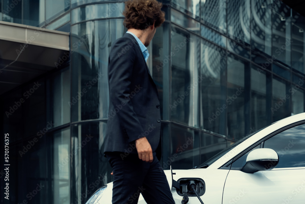 Below view of progressive businessman with electric car recharging at public charging station at mod