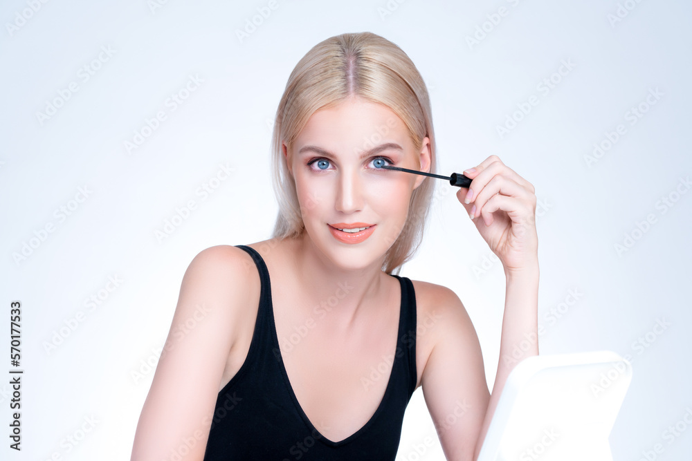 Closeup personable woman with blond hair putting black mascara with brush in hand on long thick eyel