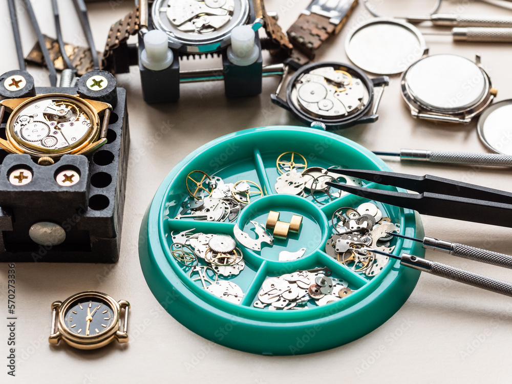 clock spare parts in tray and old watches on wooden table in watchmaker workshop