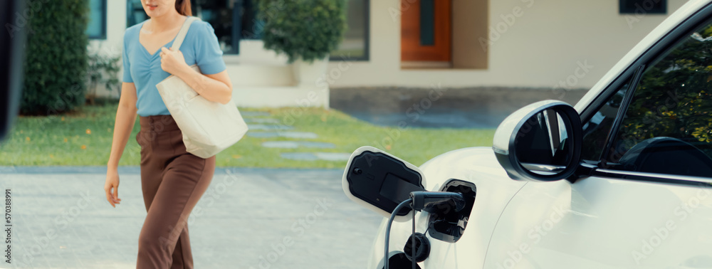 Progressive asian woman and electric car with home charging station. Concept of the use of electric 