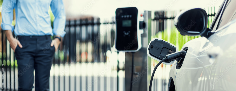 Closeup progressive suit-clad businessman with his electric vehicle recharge his car on public charg