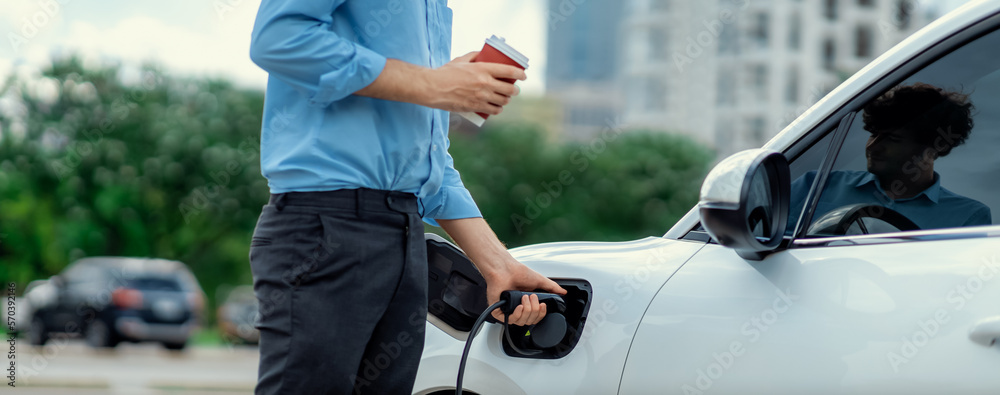 Closeup progressive man holding EV charger plug from public charging station for electric vehicle wi