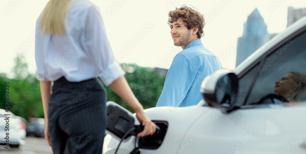 Progressive businessman and businesswoman with electric car connected to charging station before dri