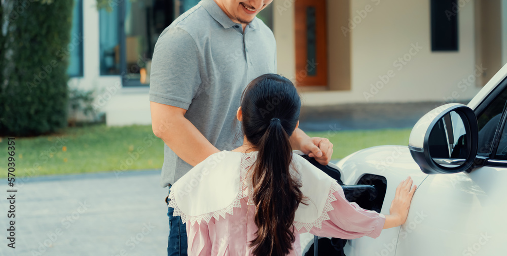 Progressive father and daughter returned from school in electric vehicle that is being charged at ho