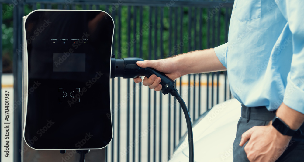 Closeup progressive man holding EV charger plug from public charging station for electric vehicle wi