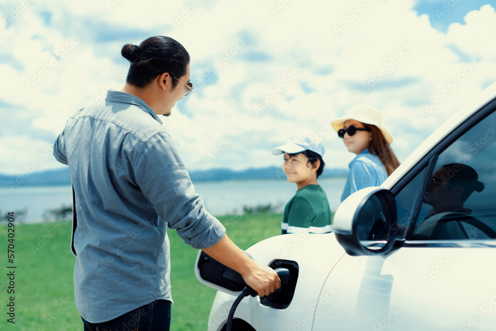 Concept of progressive happy family enjoying their time at green field and lake with electric vehicl