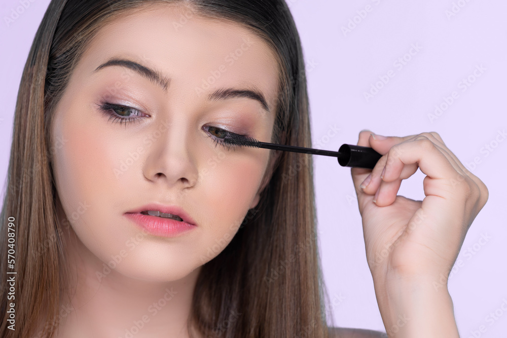 Closeup portrait of young charming applying makeup eyeshadow on her face with brush, mascara with fl