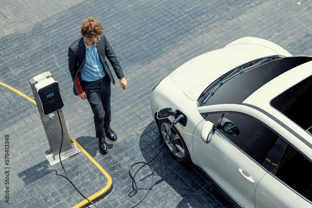 Aerial view of progressive businessman in black formal suit with his electric vehicle recharging bat