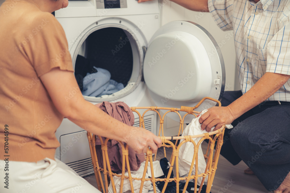 Senior couple working together to complete their household chores at the washing machine in a happy 