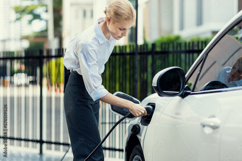 Progressive businesswoman insert charger plug from charging station to her electric vehicle with apa