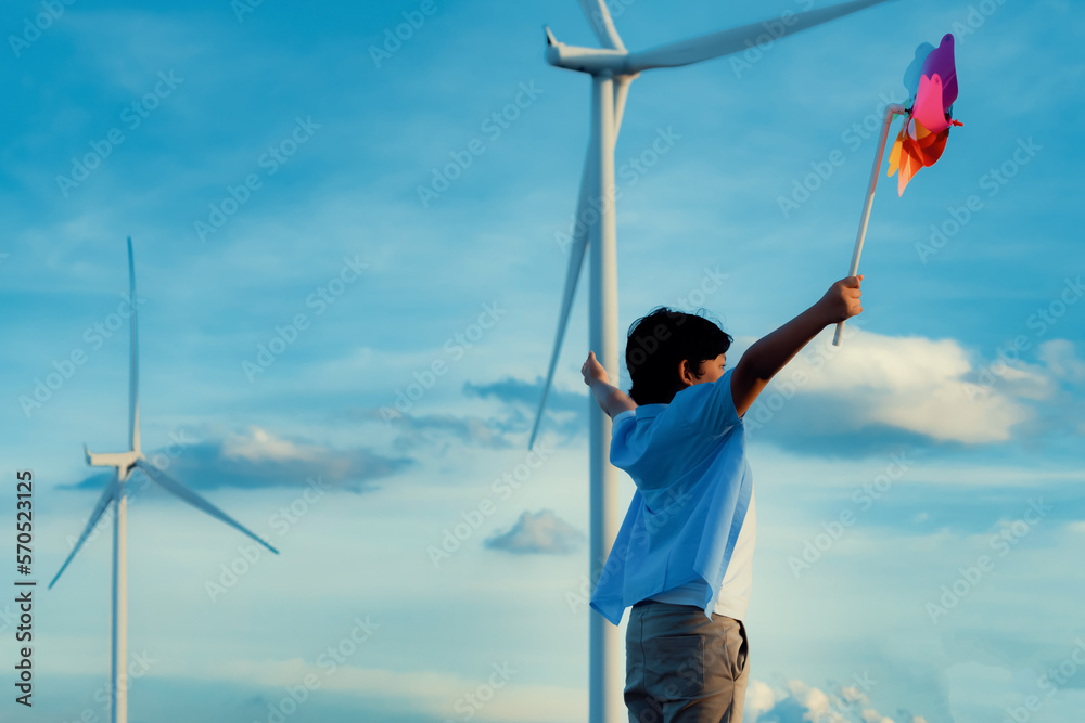 Progressive young asian boy playing with wind pinwheel toy in the wind turbine farm, green field ove