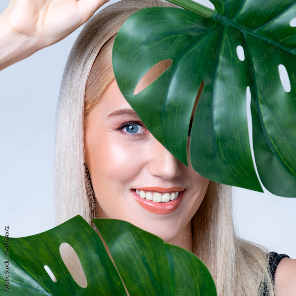 Closeup facial portrait personable woman with perfect smooth makeup holding green monstera leaves an