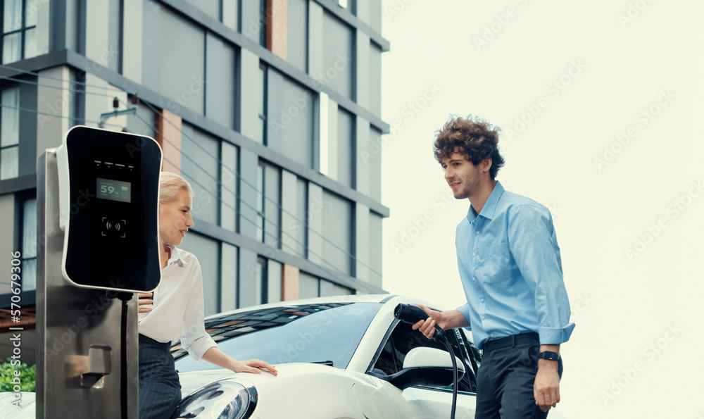 Progressive businessman and businesswoman with electric car parking and connected to public charging